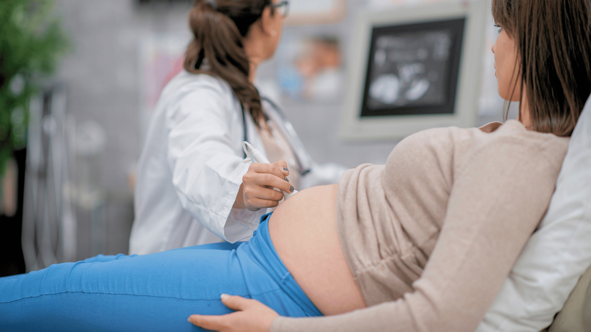 Female doctor looking at computer screen while performing an ultrasound on a pregnant woman