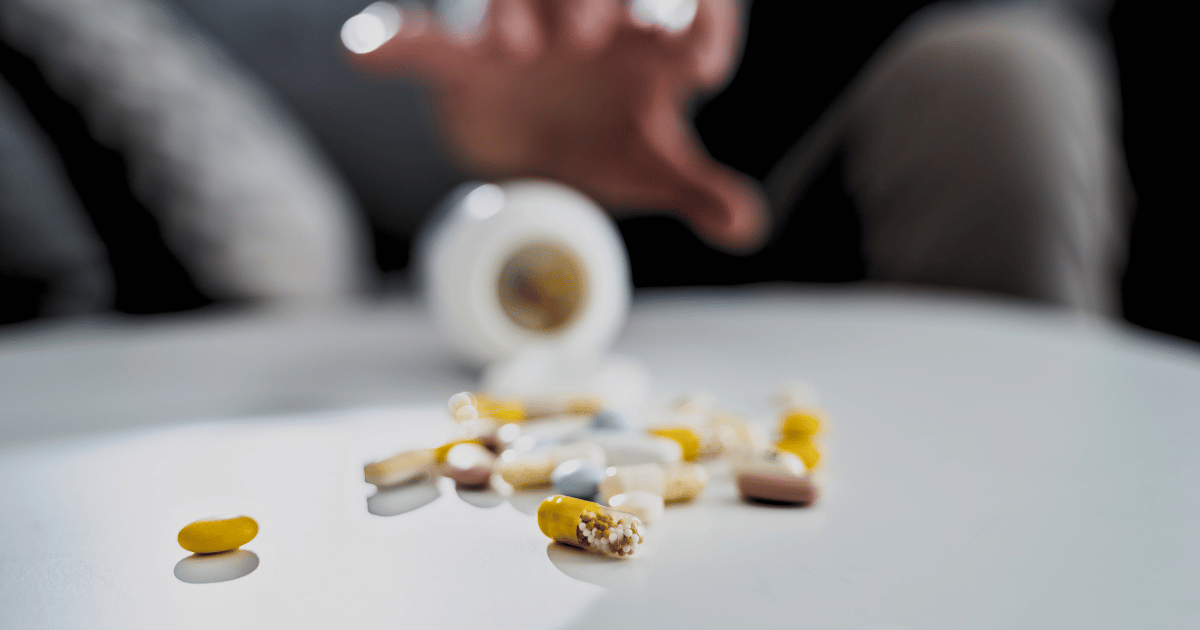 Opioid pills spilling on a table and someone reaching for them in desperation.